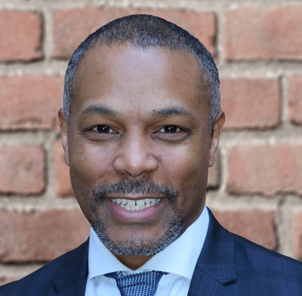 Kevin Fryar with very short black hair, wearing a navy jacket, white shirt and blue tie