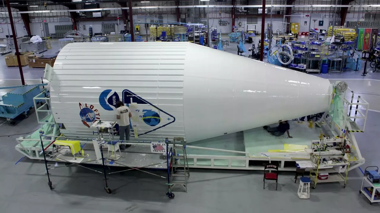 Man on scaffolding painting on a large rocket faring