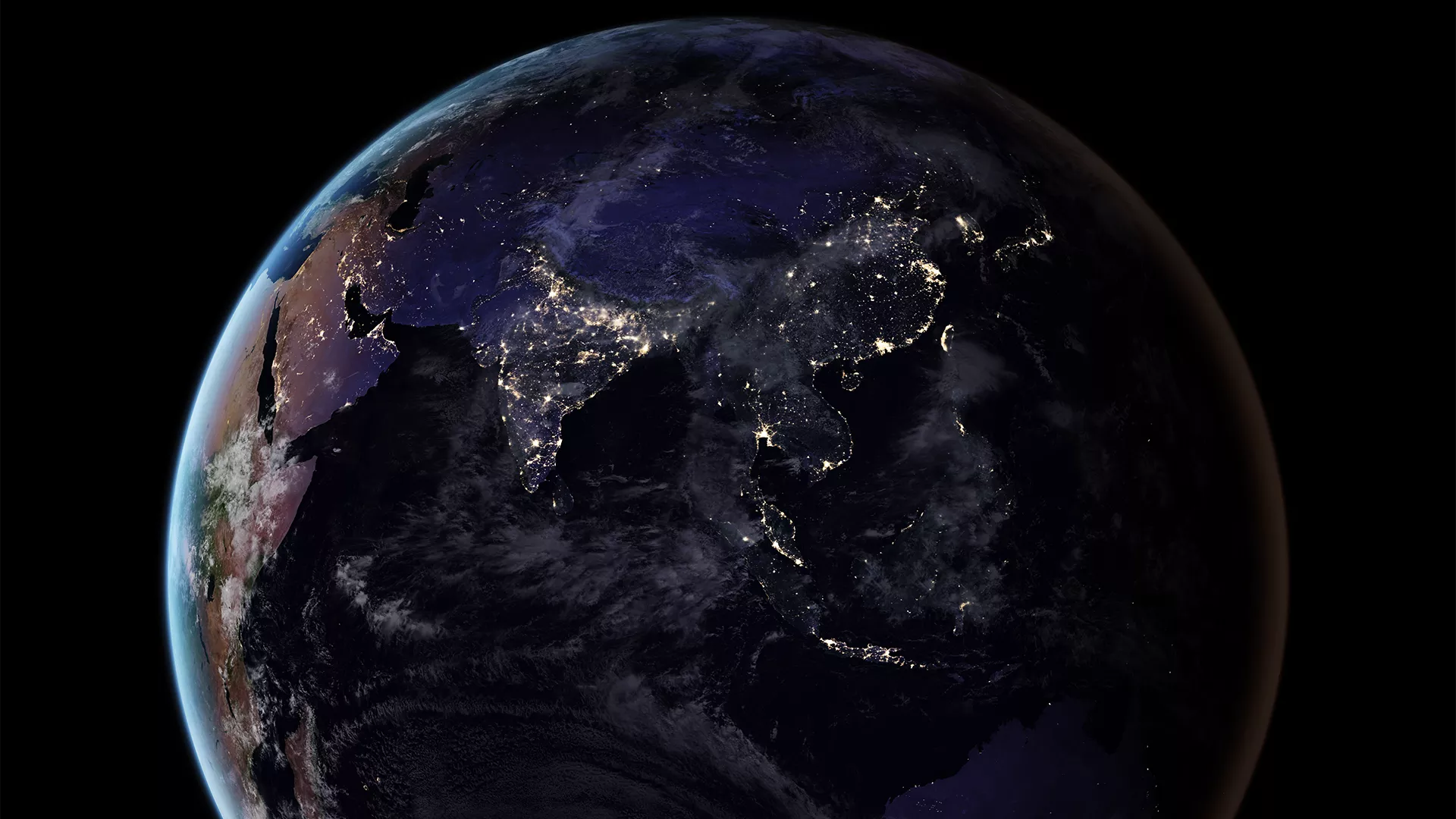 The Earth from space is in shadow and is lit up in areas with electric lights.