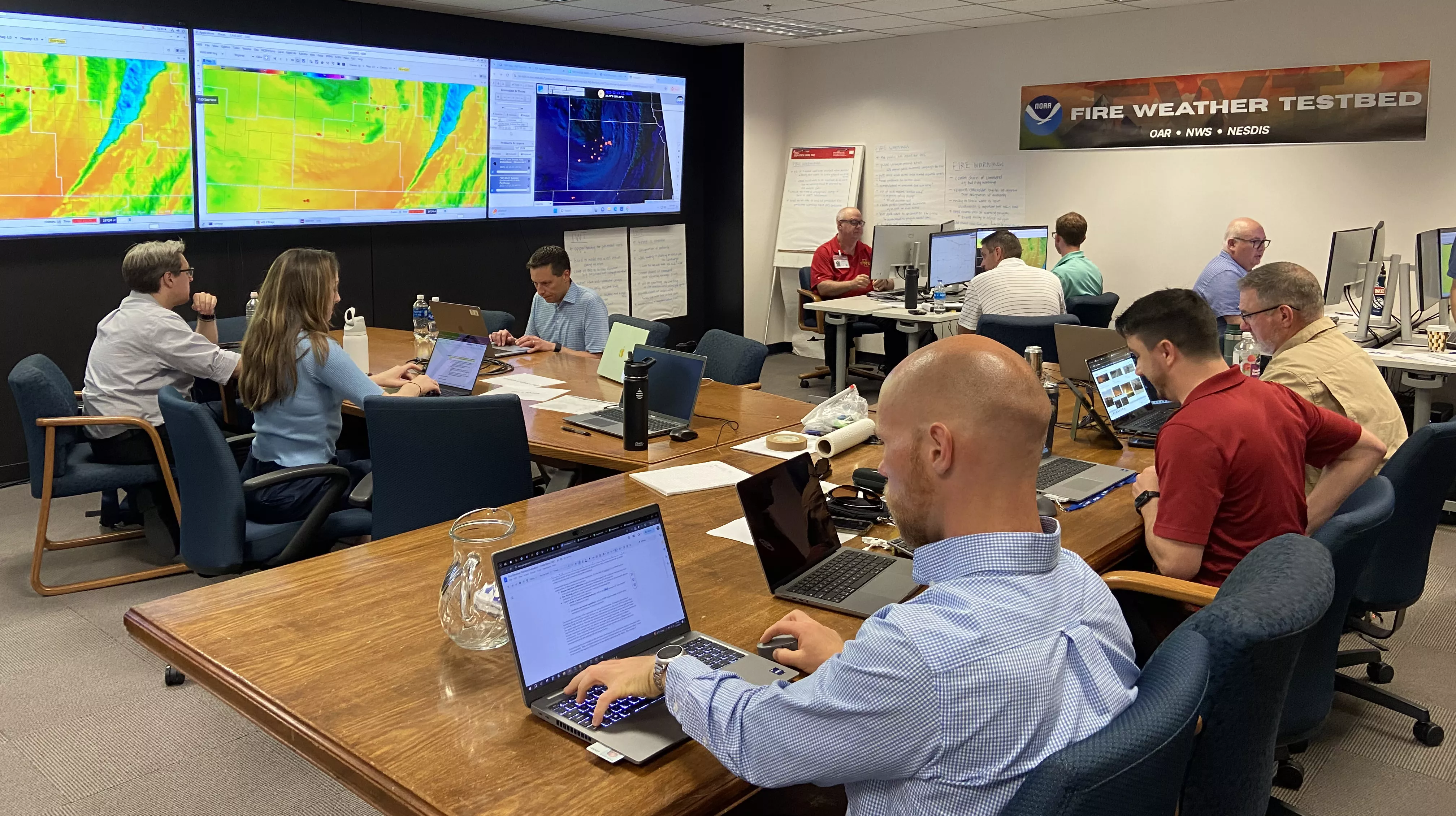 A conference room full of facilitators and researchers observed a large computer screen during a fire weather outbreak simulation of NOAA's Integrated Warning Team's fire detection and warning capabilities.