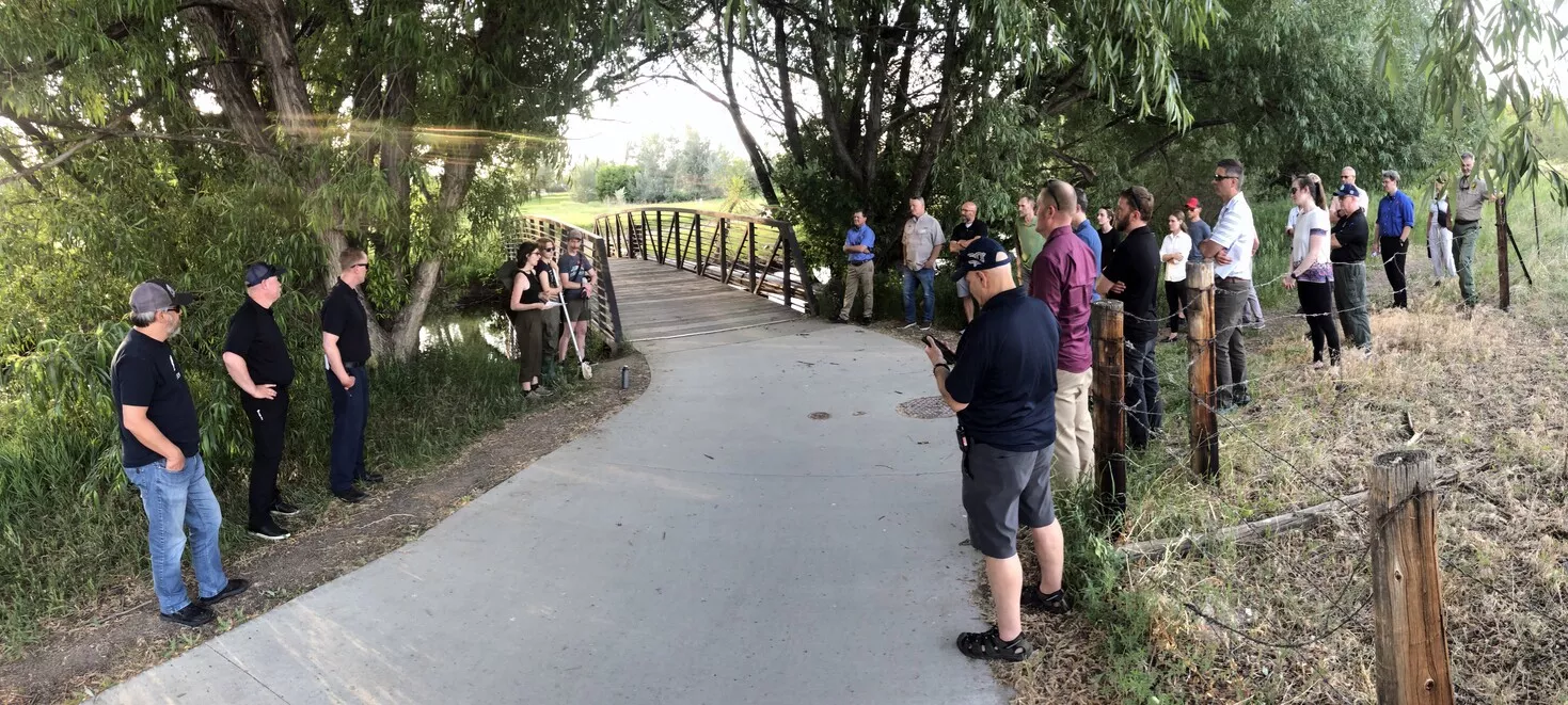 On an outdoor trail on a sunny day, a group of scientists share findings on post-fire water quality issues to partners. 