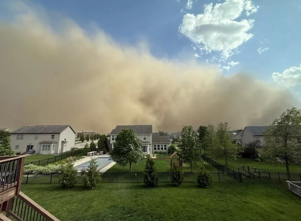 This photograph is taken in a suburban neighborhood in Bloomington, Illinois on May 16, 2025. Behind a row of houses, a large dust cloud can be seen approaching, towering into the sky.