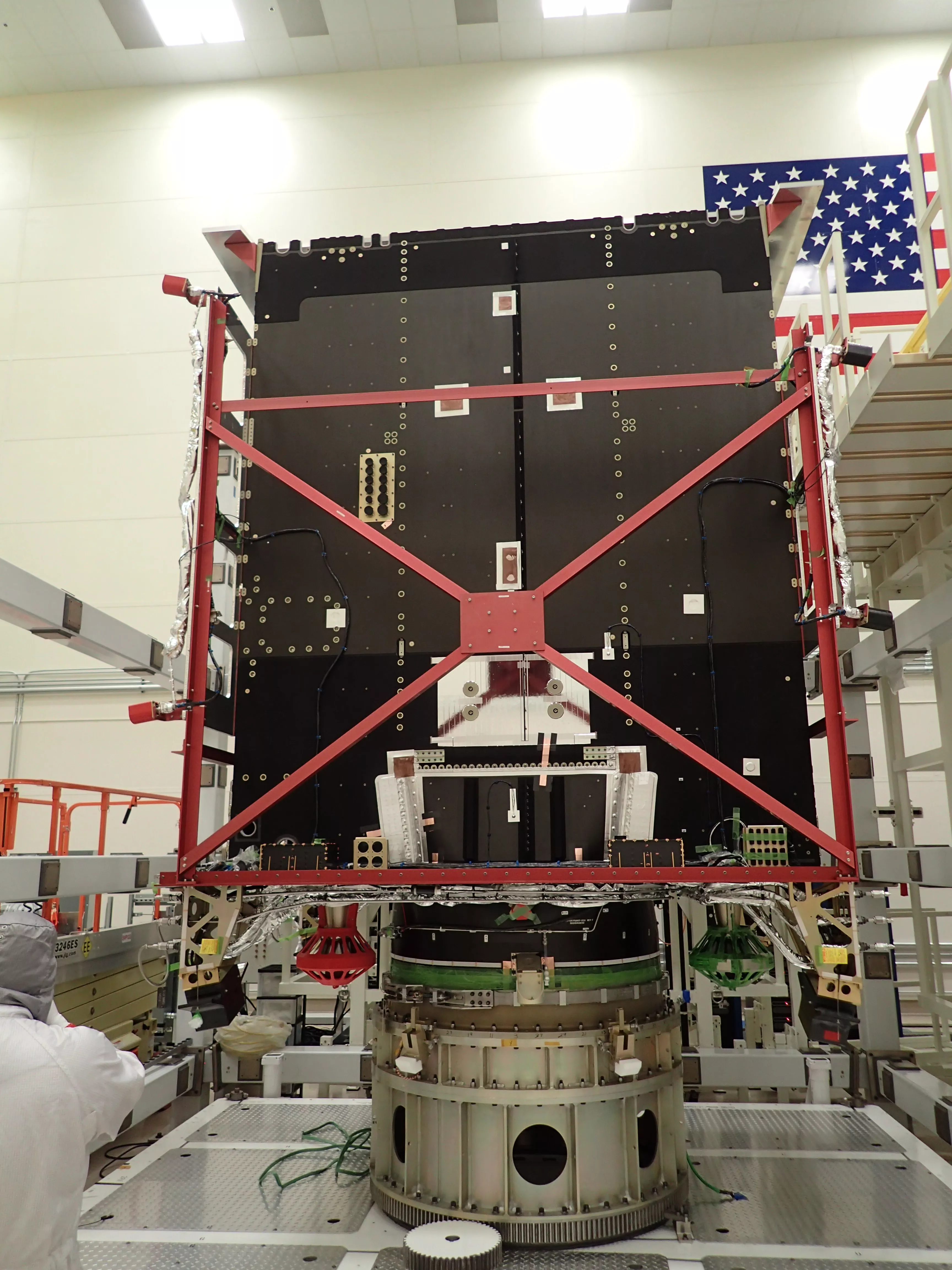 Photo of a clean room and a satellite array, with suited workers all around its perimeter.